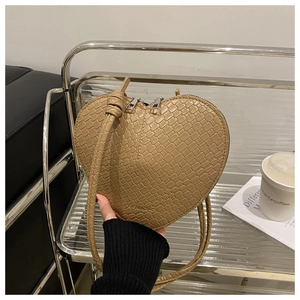 Detailed macro view of heart-shaped beige crossbody bag with silver zipper and leather strap