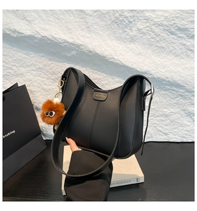 Gros plan d'un sac seau en cuir noir avec texte doré et charmant petit monstre marron