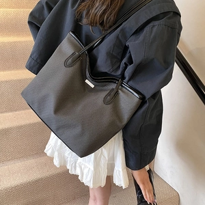 Chic black woven tote bag with silver logo worn on shoulder for stylish daily commuting