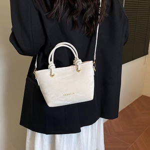 White bucket bag with gold Fashion text and knotted handle worn as a crossbody bag