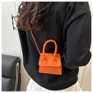Close-up of orange mini leather handbag with large curved handle shown on a model