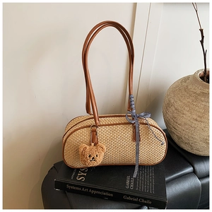 Detail of woven straw handbag with brown leather handles and a cute bear charm