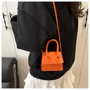 Detail of a mini orange trapezoid leather handbag featuring a curved top handle and shoulder strap