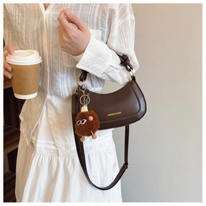 Detail of dark brown crescent bag with gold zipper and a cute plush monster charm