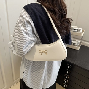 Minimalist white crescent underarm bag with gold bow clasp shown on a model shoulder
