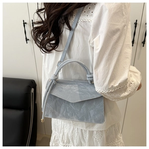Model draagt een lichtblauw-grijze crossbodytas met marmertextuur en gouden hardware