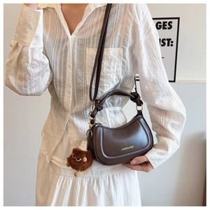 Detail of dark brown leather crescent bag with cute plush monster charm accessory