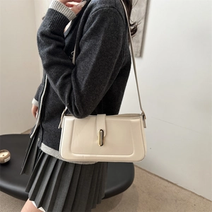 Minimalist beige shoulder bag with a sleek gold buckle, shown in a stylish 2025 lifestyle setting