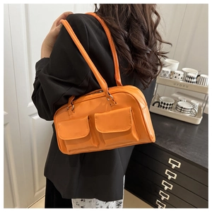 Detail view of bright orange tote bag with front flap pockets on a black suit model