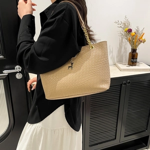 Fashion woven tan tote bag with gold chain strap and deer charm on a model