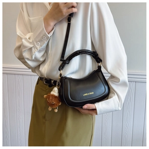 Close-up of black PU leather crescent bag with gold logo and brown plush pendant charm