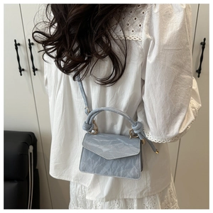 Dettaglio mini borsa azzurra con texture plissettata, manico a nodo e finiture dorate