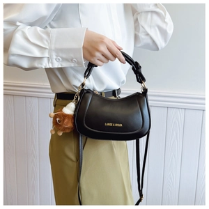 Detail of black crescent shoulder bag with gold logo and brown plush doll charm