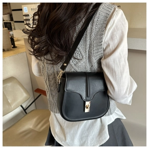 Model showing a black matte leather shoulder bag with gold square lock in a cafe setting