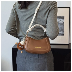 Detailed view of caramel crescent bag with cream strap and plush charm on female model