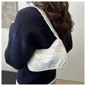 Detail of white baguette bag with colorful stitching and embossed texture on model