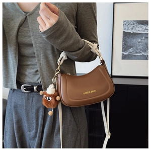 Brown crescent bag with white knot handle and plush monster charm shown on shoulder