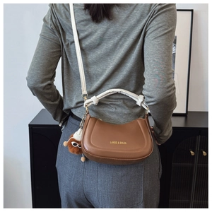 Brown leather crescent shoulder bag with white handle and plush doll charm detail