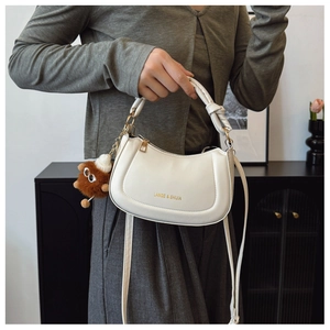 Detail of cream crescent bag featuring knotted handle and plush monster charm accessory