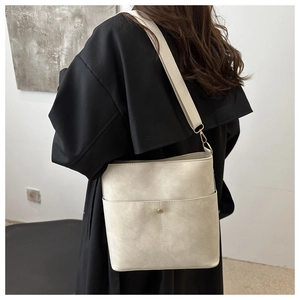 Detailed view of off-white leather bucket bag with gold accents and wide shoulder strap