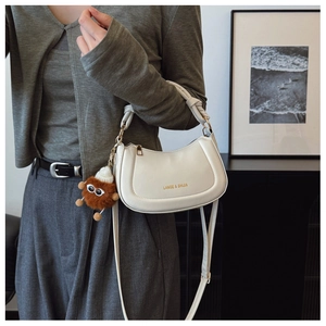 Detailed shot of white leather crescent bag with woven handle and plush monster charm