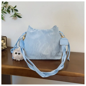 Light blue bucket bag with pleated texture, woven strap and plush charm on wood table