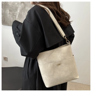 Detail of beige textured leather bucket bag with gold hardware on black coat
