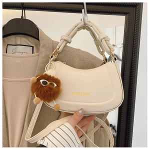 Detail of cream crescent hobo bag with knotted handle and plush monster charm decoration
