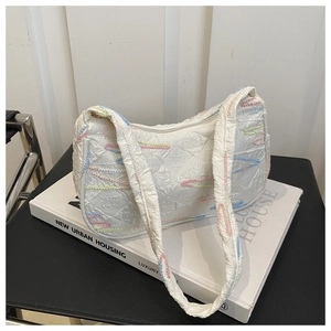 Close-up of cream white shoulder bag featuring geometric textures and colorful embroidery