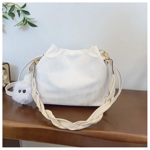 Detail of white pleated bucket bag with broad woven strap and plush monster charm