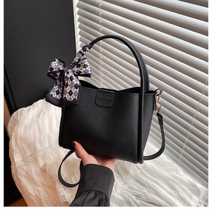 Detail der schwarzen Handtasche aus Kieselleder mit modischem Logo und karierter Schleife