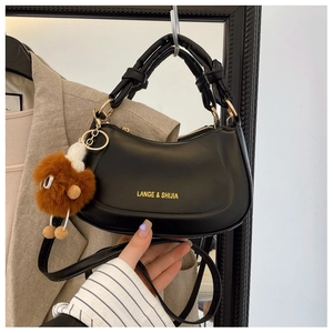 Detail view of black leather crescent bag with gold logo and brown plush charm