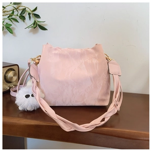 Pink pleated bucket bag with a woven strap and plush monster charm on a wooden desk