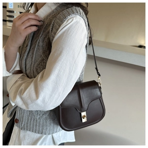 Dettaglio borsa a sella marrone scuro vintage con fibbia dorata indossata da una modella