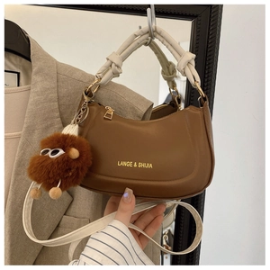 Close-up of brown crescent crossbody bag with white woven handle and plush charm detail