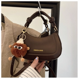 Detail of hobo bag with knotted handle, gold hardware, and plush doll charm accessory