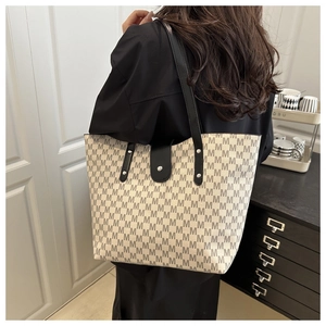 Detail of a large beige tote bag with M-pattern print and black leather shoulder straps