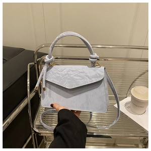 Detail van de lichtblauwe crossbodytas met rimpeltextuur en decoratief knoopdetail aan handvat