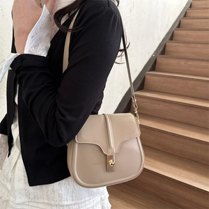 Borsa a sella beige minimalista con chiusura a scatto dorata indossata da una modella