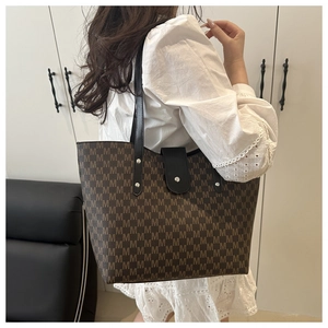 Brown monogram tote bag with black leather straps and silver rivets on female model