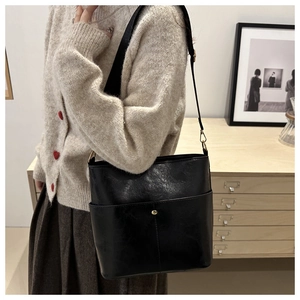 Chic black bucket shoulder bag with gold metal buckle detail on a model in home setting