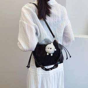 Minimalist black drawstring bucket bag with woven handle and plush monster charm