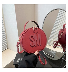 Close-up of red round crossbody bag with SM logo and textured synthetic leather detail