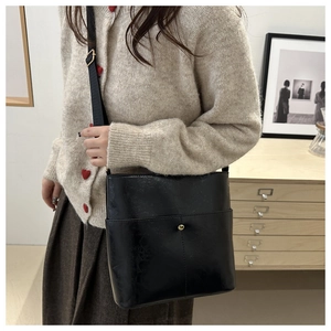 Detail of black glossy bucket bag with metal buckle and adjustable strap on a shoulder