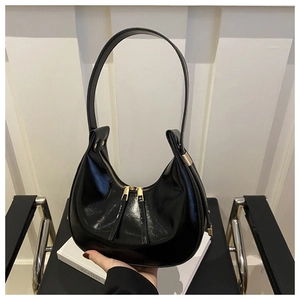 Detailed view of black patent leather crescent bag with gold zipper and stud accents