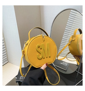 Macro detail of round yellow leather bag with 3D SM logo and metallic gold zipper