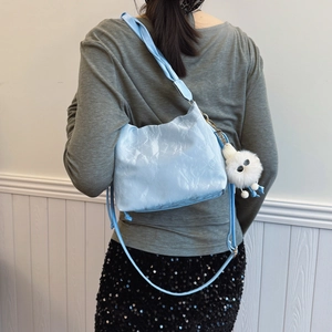 Light blue pleated bucket bag with plush charm shown on a model in a minimal setting