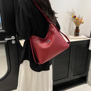 Red woven hobo tote bag with silver bow charm shown on model in an elegant home setting