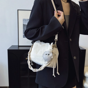 Chic cream bucket bag with braided handle and plush charm on a model in a modern room