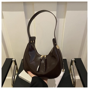 Detail of dark brown polished leather crescent hobo bag with gold hardware on a chair